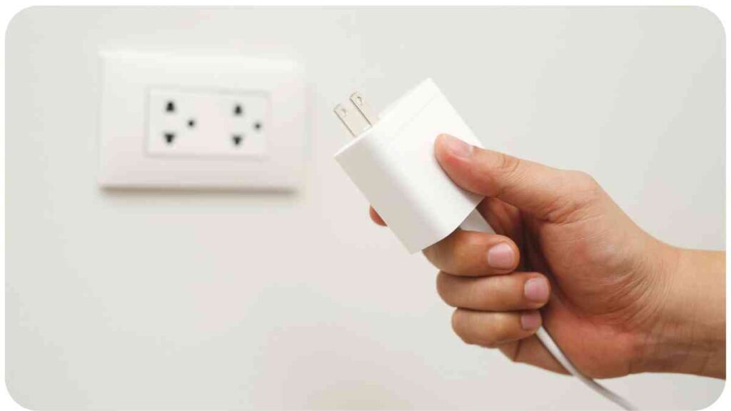 a hand is holding a white plug in front of a wall outlet